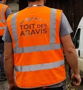 Couvreur du Toit des Aravis de dos, gilet orange au logo de l'entreprise, sur un chantier à Entremont