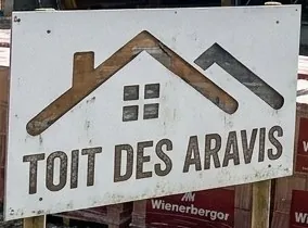 Panneau Toit des Aravis planté devant un chantier de grange dans le Borne